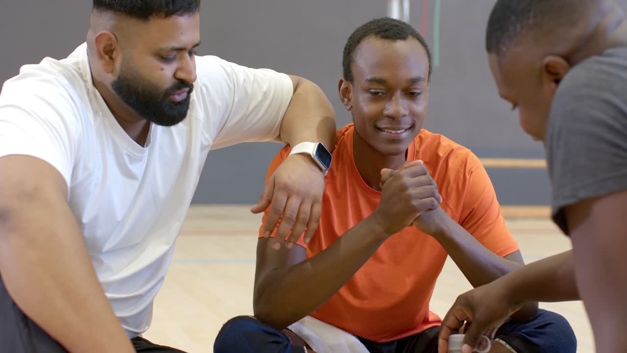 Break from game driving diverse male friends discussing tactics on sports court using smartwatch