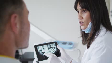 Dentista-Birracial-Con-Mascarilla-Examinando-Los-Dientes-De-Un-Paciente-Masculino-En-Una-Clínica-Dental-Moderna