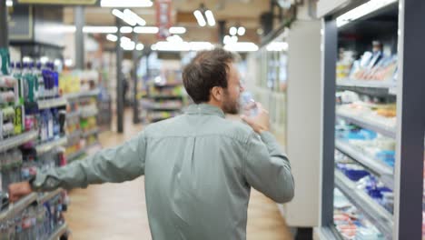 Mann-Im-Supermarkt-Tanzt-Und-Benutzt-Eine-Flasche-Wasser-Als-Mikrofon.-Positive-Tänze-Im-Und-Leeren-Lebensmittelladen