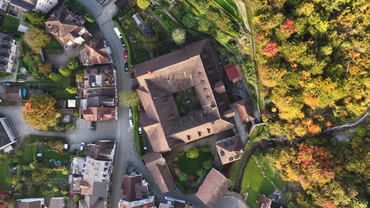 Top-down aerial view of a square, brown-roofed building complex surrounded by a small town and vibrant autumn foliage in Walenstadt, Schweiz