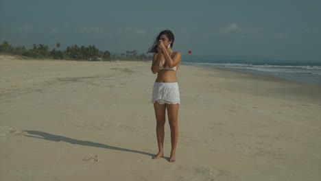 handheld full length clip of woman applying suntan lotion to arms and hands, on sandy beach in summertime