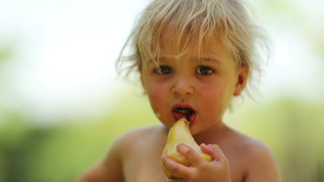 candid portrait of blonde baby infant eating pear fruit outdoors in the sunlight. 4k clip resolution of child eating food outside