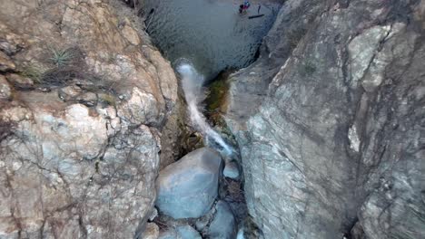 topdown eaton canyon falls, drone ascending motion revealing water flowing down rocky cliff waterfall with tourists