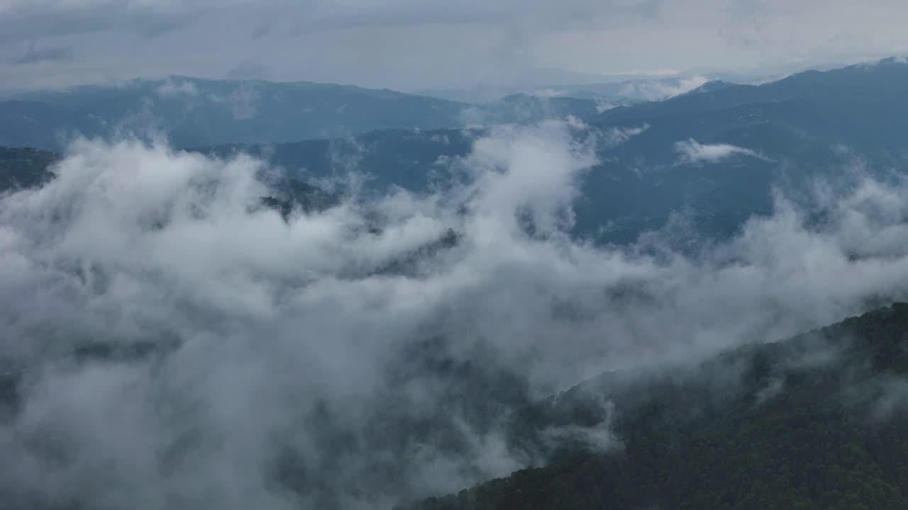 Aerial drone shot flying over clouds resting gently on mountaintops at dawn.
