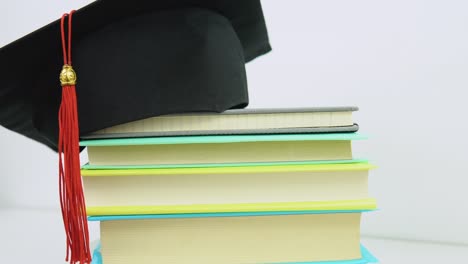 a black square graduate hat with a red tassel lies on a stack of books. objects rotate around their axis on the stand. education concept