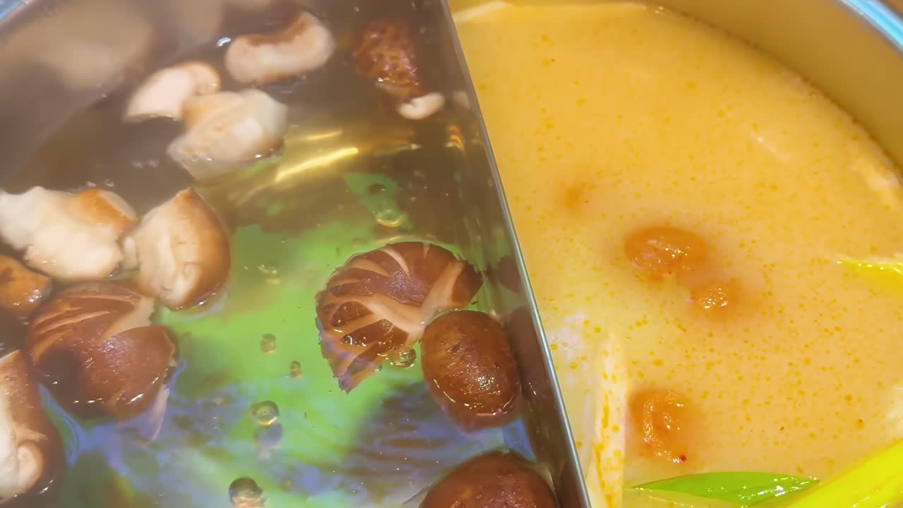 Close-up of mushrooms simmering in a divided hotpot with rich broth and vibrant greens.