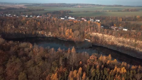 Eine-Antenne-Eines-Ruhigen-Sees,-Umgeben-Von-Bäumen-Und-Vegetation-Mit-Einigen-Häusern-Im-Hintergrund-Unter-Einer-Majestätischen-Goldenen-Stunde