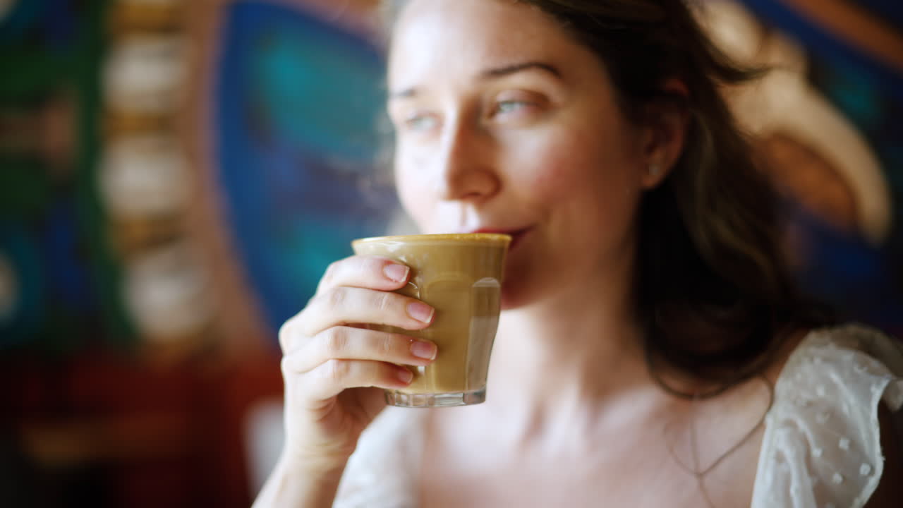 Brunette woman in white dress drinking a coffee at a cafe in daylight