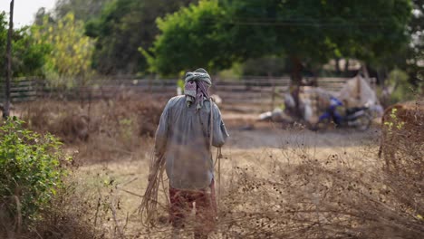 indian farmer walking through a dry field carrying a rope