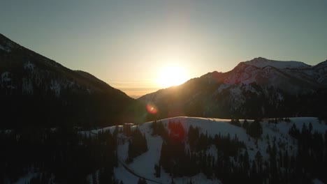 Drone-Sobre-La-Brillante-Puesta-De-Sol-En-Las-Cimas-De-Las-Montañas-Nevadas-En-Brighton,-Utah