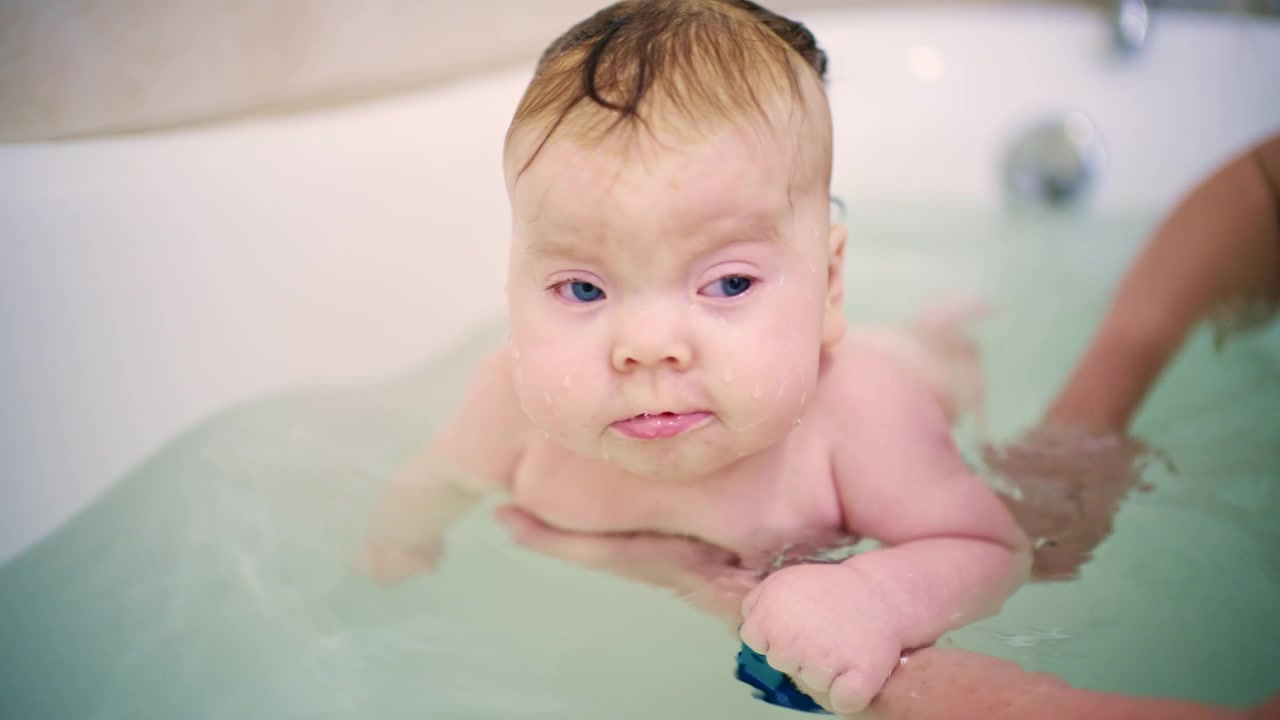 Primeiro plano de um bebê sendo apoiado por um adulto durante o banho