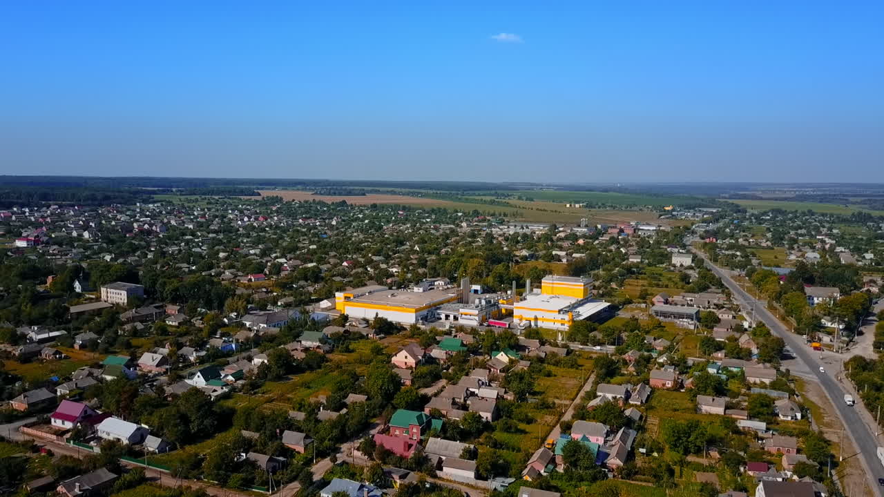 Flying above the provincial town with private cottages. Farmlands and forests at backdrop. Aerial view.