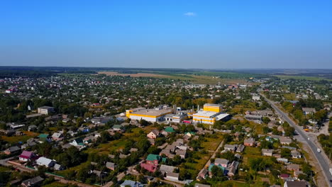 Flying above the provincial town with private cottages. Farmlands and forests at backdrop. Aerial view.