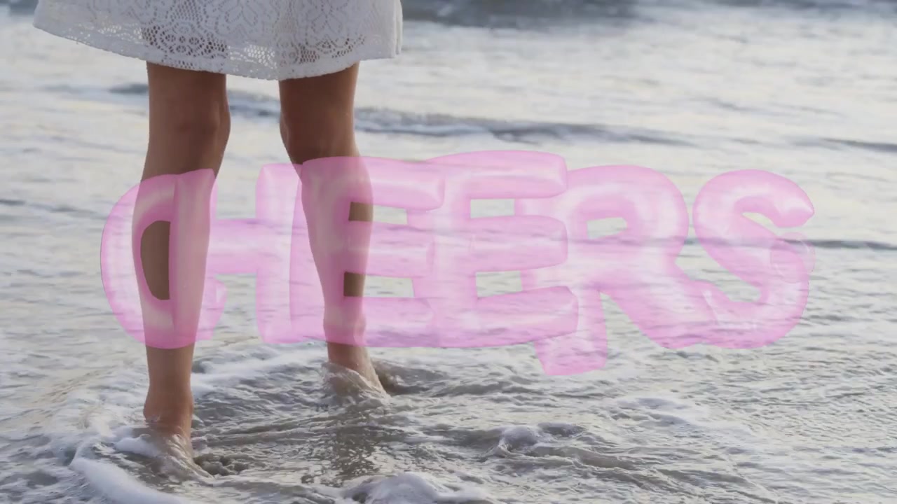 Donna che sente le onde lambire i piedi, camminando lungo la spiaggia sentendo la risacca, con sovrapposizione rosa "CHEERS" sulle gambe