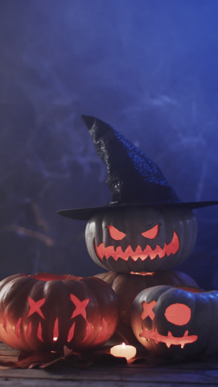 Verticale video van uitgesneden Halloween-pompoenen en rook met ruimte voor tekst op blauwe achtergrond