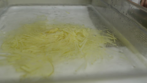 Putting-potato-shreds-into-a-tray-with-ice-after