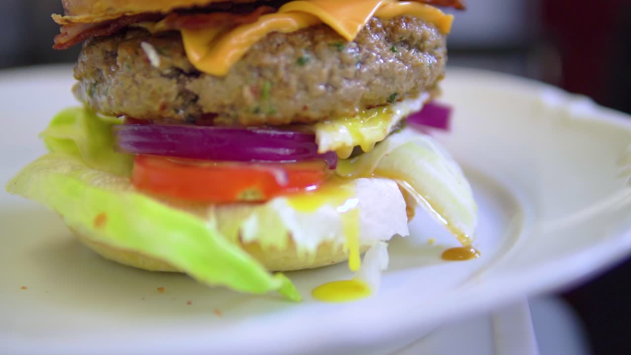 hamburguesa lista para comer directamente de la parrilla con huevo fluyendo sobre la lechuga en cámara lenta