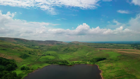 Aerial-shot-of-a-tarn-or-lake-surrounded-by-hills-and-mountains-on-a-bright-sunny-day