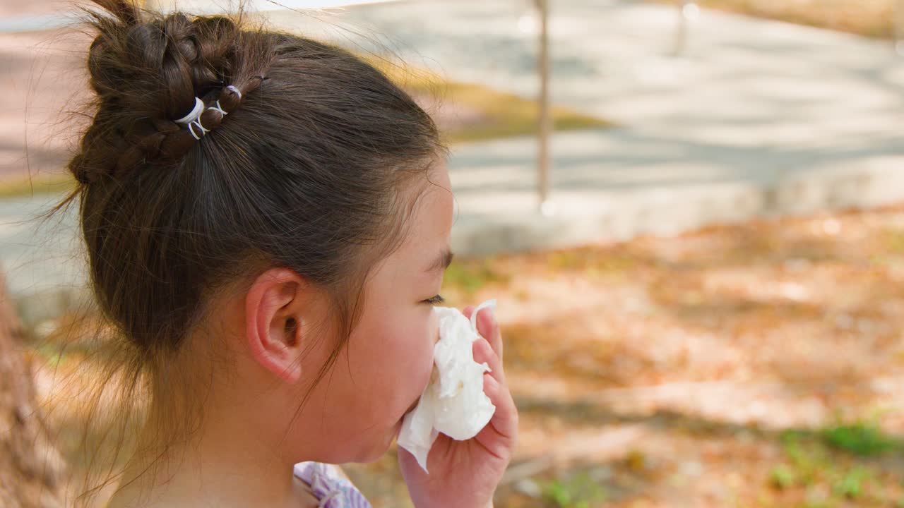 Una madre pulisce delicatamente il viso della figlia con un fazzoletto bianco in un parco soleggiato.