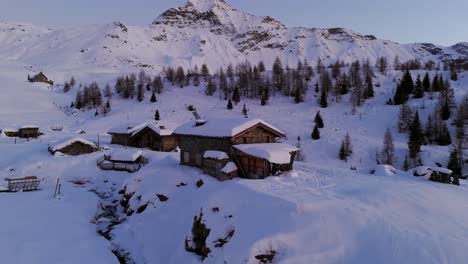 snowy landscape with wooden huts in valmalenco dolomites mountains at sunset in valtellina, italy