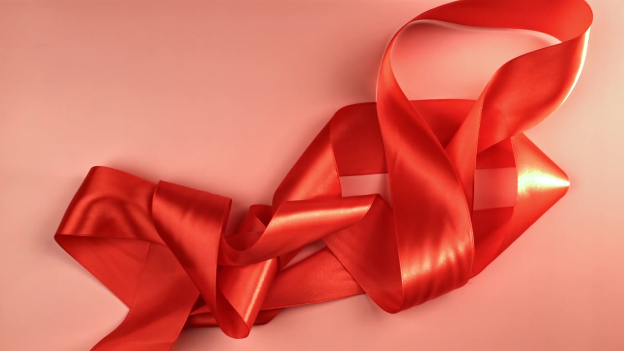 Elegantes rotes Satinband legt sich langsam auf eine rosa Oberfläche.