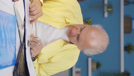vertical video of home office worker old man looking at the file angrily.
