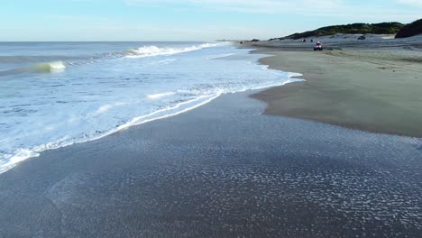 low flying drone shot on the beach following the waves hitting the sand with a beautiful sky in the back