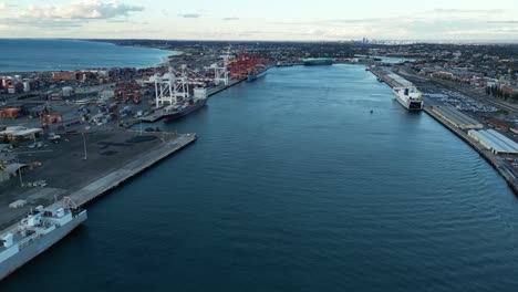 tiro aéreo hacia adelante sobre el río con el puerto industrial de fremantle con grúas y contenedores en la ciudad de perth, australia