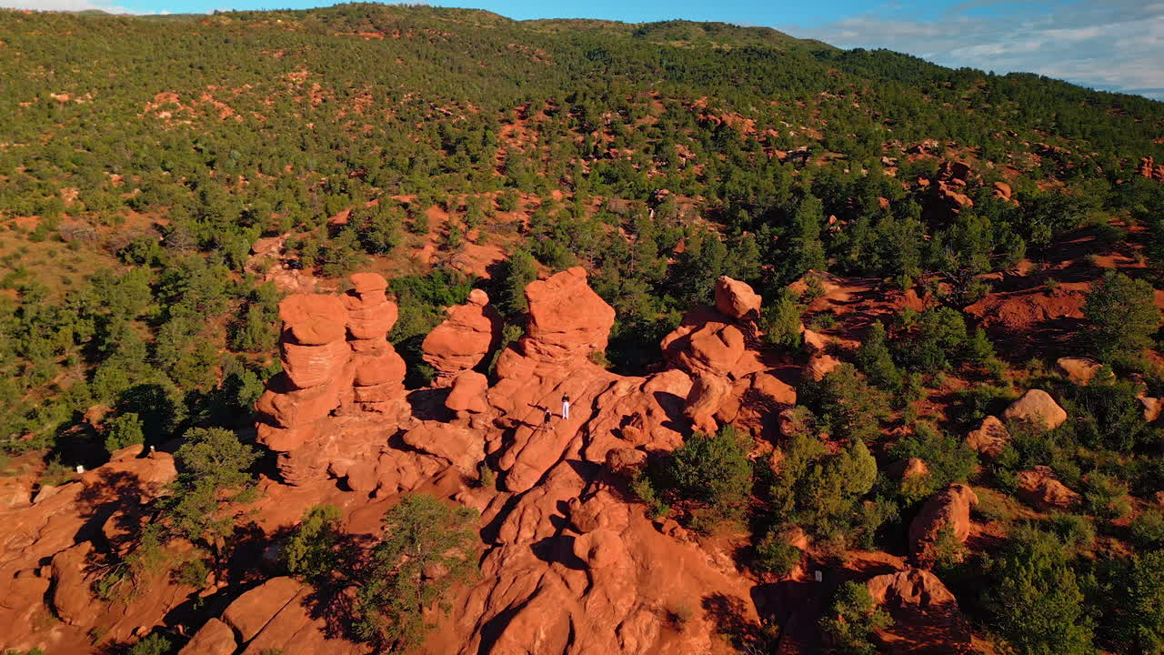 Approaching two people standing on the whimsical red rocks on sunny day. Aerial perspective on the amazing rock formations in Garden of the Gods Park, Colorado Springs, Colorado, USA