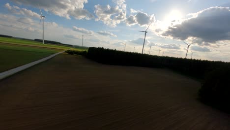 FPV-flying-toward-wind-turbines-on-sunny-day,-aerial-view