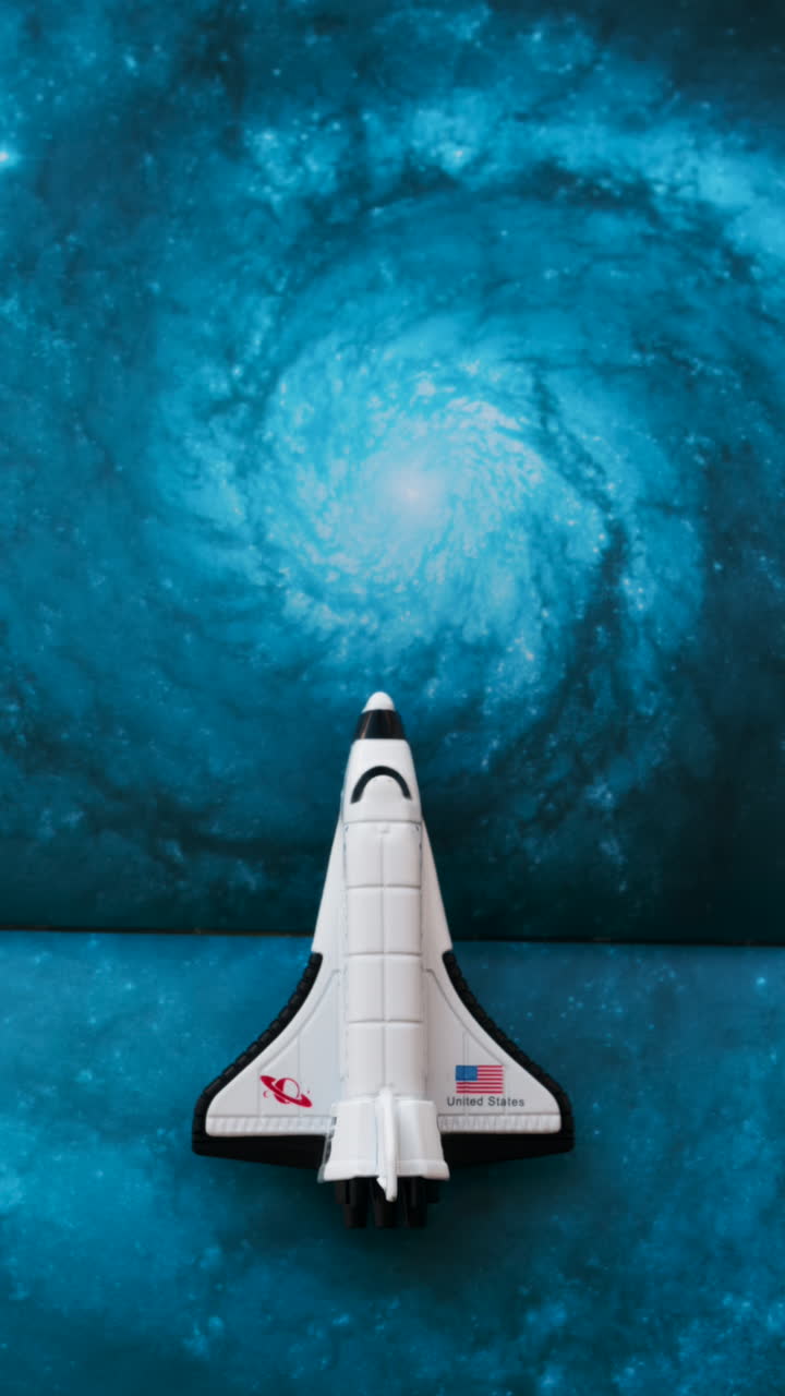Close up of a miniature toy space shuttle placed on a blue cosmic galaxy backdrop