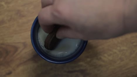 Hand-dunking-cookie-into-mug-of-milk-flat-lay-close-up