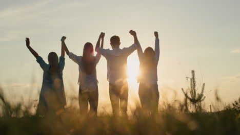 silueta de un grupo de amigos - levantar las manos contra el telón de fondo del sol poniente. trabajo en equipo y concepto de éxito