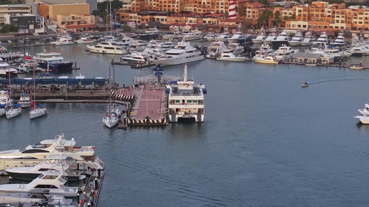 Scatto aereo con teleobiettivo di un gigantesco traghetto passeggeri con persone a bordo e yacht di lusso che lo circondano nel porto turistico di Los Cabos, Messico, al tramonto.