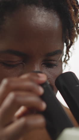 african american woman looks at viruses through microscope on blurred background. female student provides medical research in modern laboratory closeup