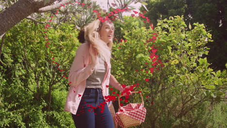 Animation-of-red-heart-over-happy-diverse-couple-walking-with-picnic-basket-in-sunny-garden