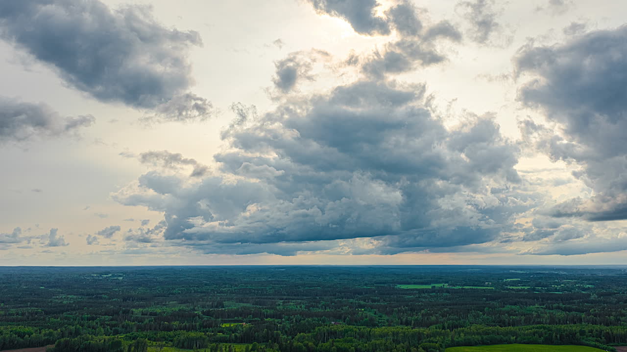 Storm clouds gather and flow over sunny green landscape and open farmland, dramatic and moody lighting