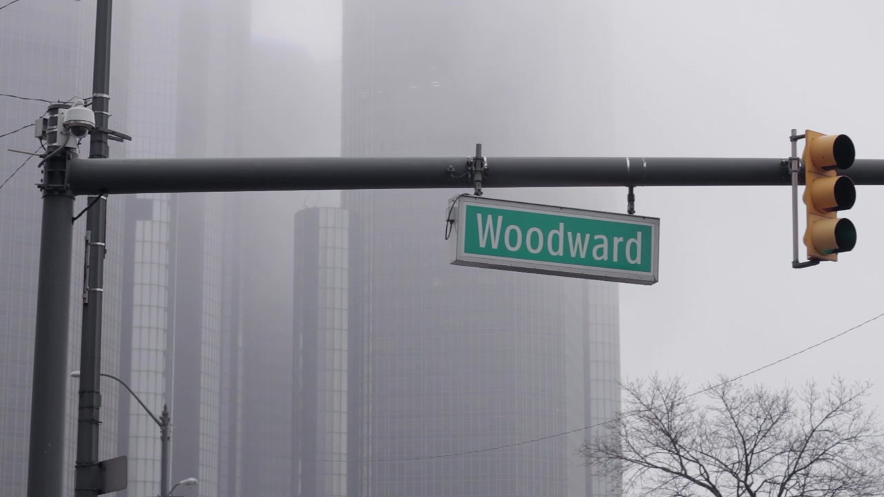 Woodward Avenue sign in front of the GM Headquarters in Downtown Detroit, Michigan on a cloudy day.