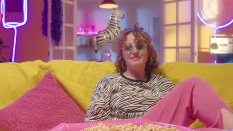 young woman watching a movie with popcorn on a yellow sofa