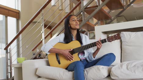 Frau-Mit-Gemischter-Abstammung-Sitzt-Zu-Hause-Auf-Der-Couch-Und-Spielt-Gitarre-Und-Singt