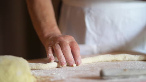 mother at home rolling fresh dough for italian gnocchi with