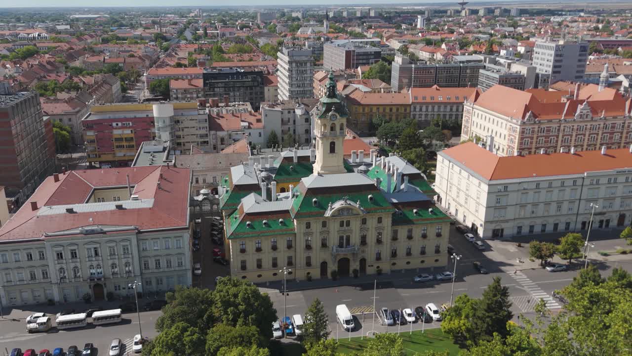 Aerial approaching Szeged City Hall, flying above the park, showcasing historic architecture and lush urban greenery