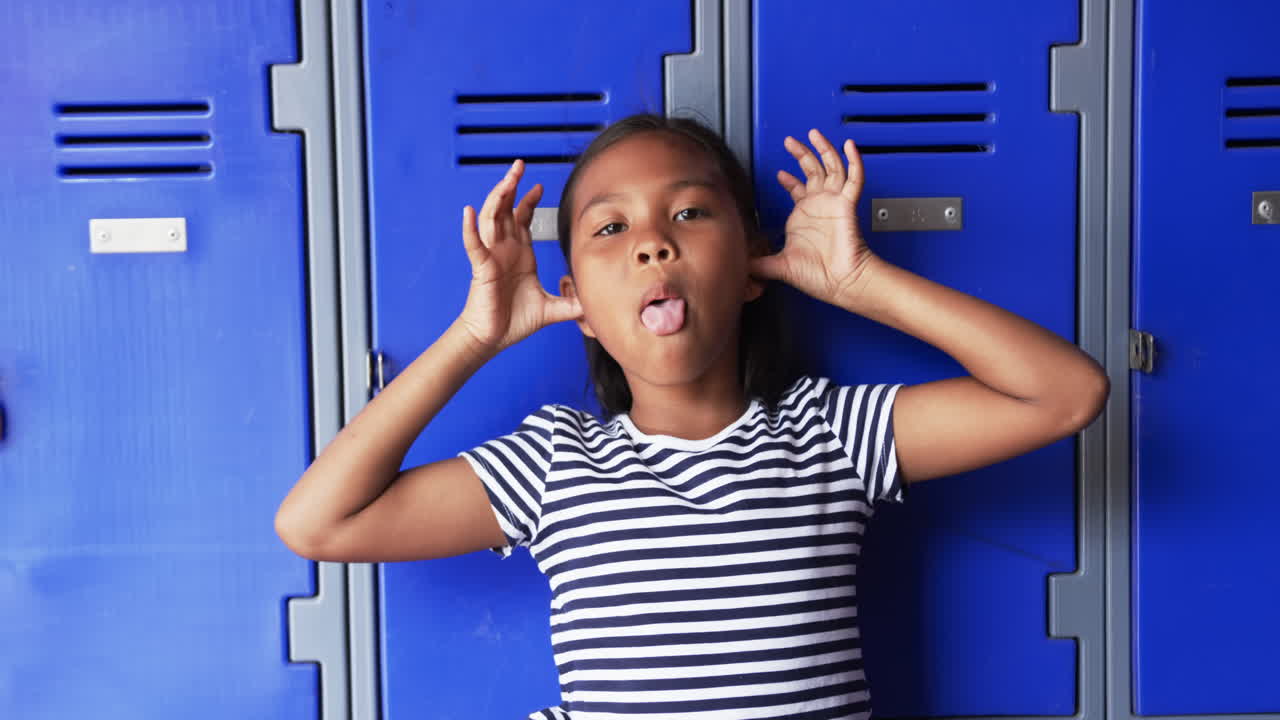 In a school hallway, a young biracial girl makes a playful face