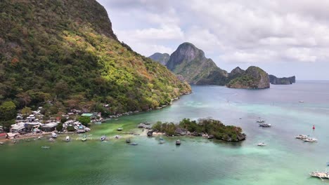 tropical coastline in el nido, palawan with turquoise waters, scattered boats, small village, and lush limestone cliffs under partly cloudy skies in a scenic, tranquil island setting