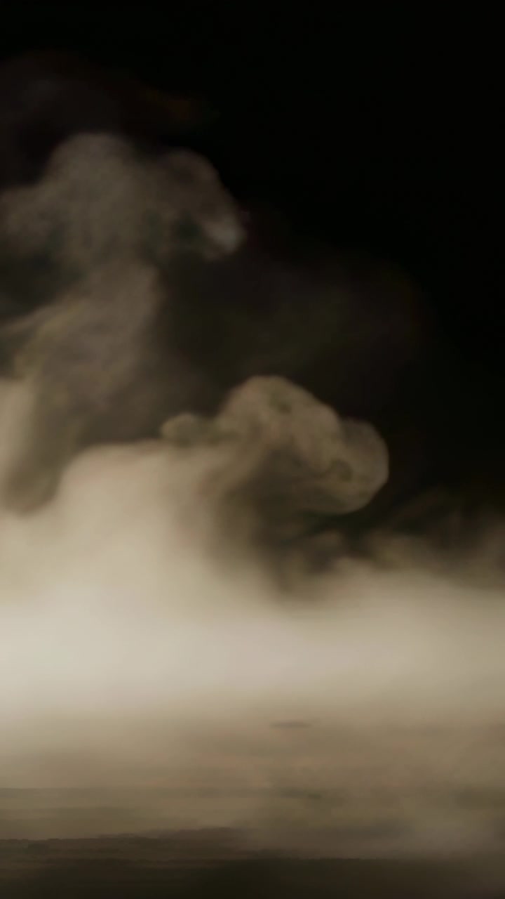 Video verticale: Una massa di vapore bianco che sale, avvolgendosi a spirale attraverso uno studio buio, con luce diffusa