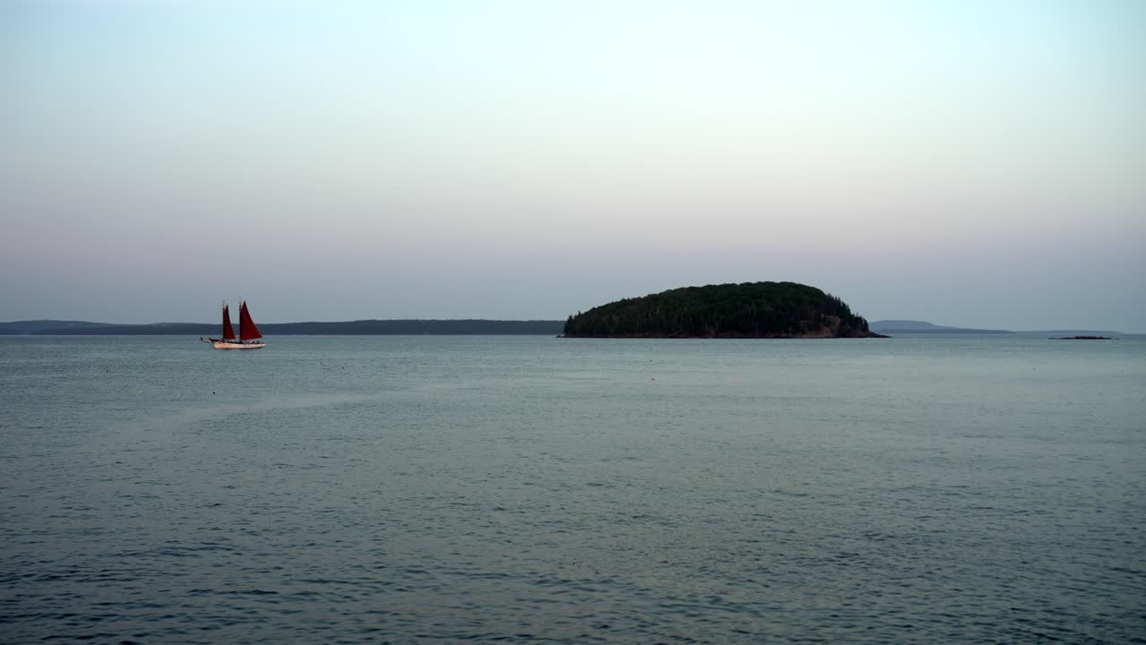 중간 왼쪽에 있는 선박은 부드러운 해가 지는 하늘 아래 물을 가로질러 느린 속도로 항해합니다.