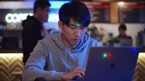 focused individual engaged in work on laptop in cozy coffee shop with neon lights and a relaxed atmosphere