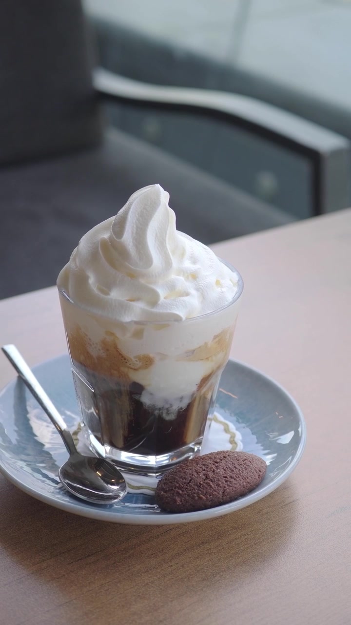 Vaso de café helado con nata montada y galleta.