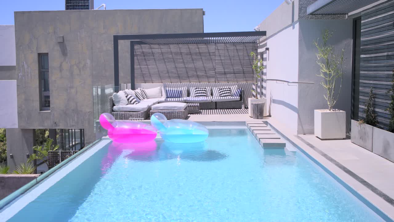 Two inflatable floats drifting across rooftop pool under gentle breeze, showing pergola and sofa