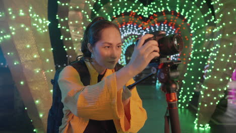 a woman is using a video monopod in a park with tunnel light display at the background